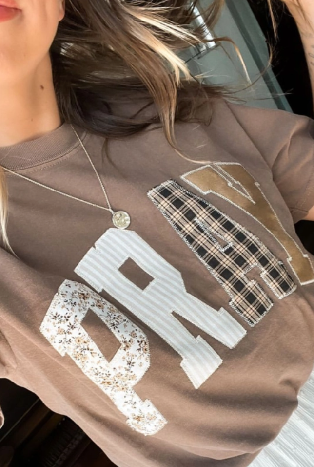 Tan t-shirt with 'PRAY' text in various patterns like patchwork.