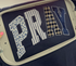 Navy blue t-shirt with 'PRAY' text in various patterns like patchwork.